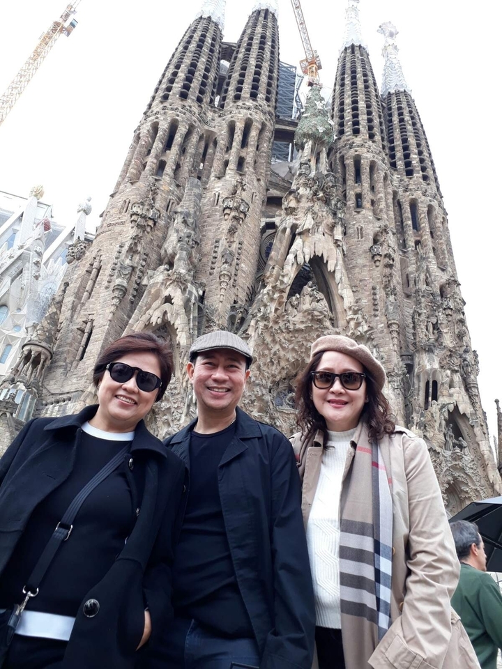 Trois personnes posant devant la façade d'un grand bâtiment complexe.