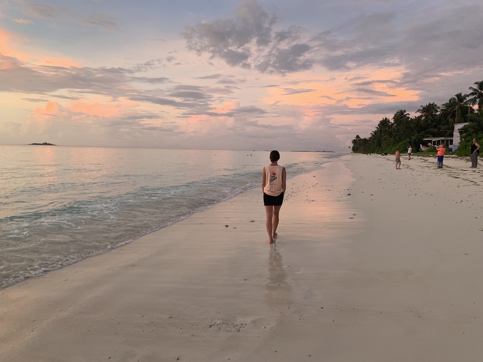 Persona caminando por una playa serena al atardecer.