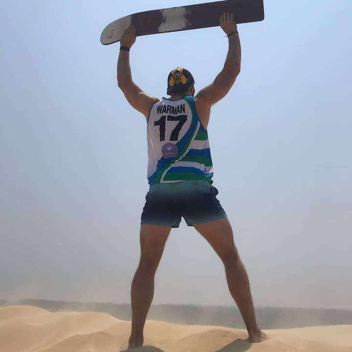 Person jumping on a sand dune with hands up.