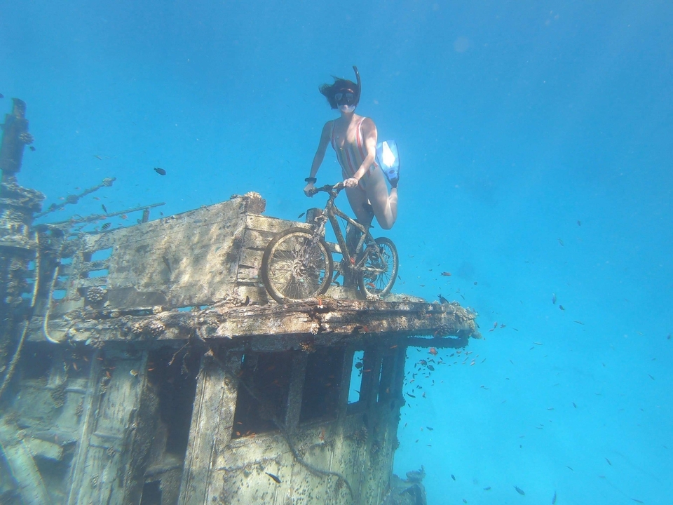 Persona haciendo snorkel bajo el agua en una bicicleta hundida.