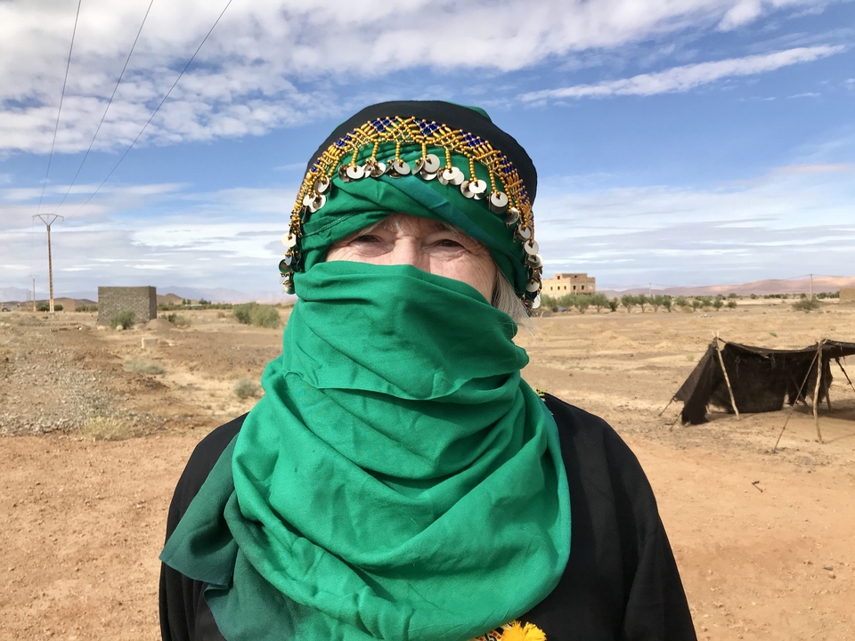 Woman in traditional attire with a green scarf in a barren landscape.