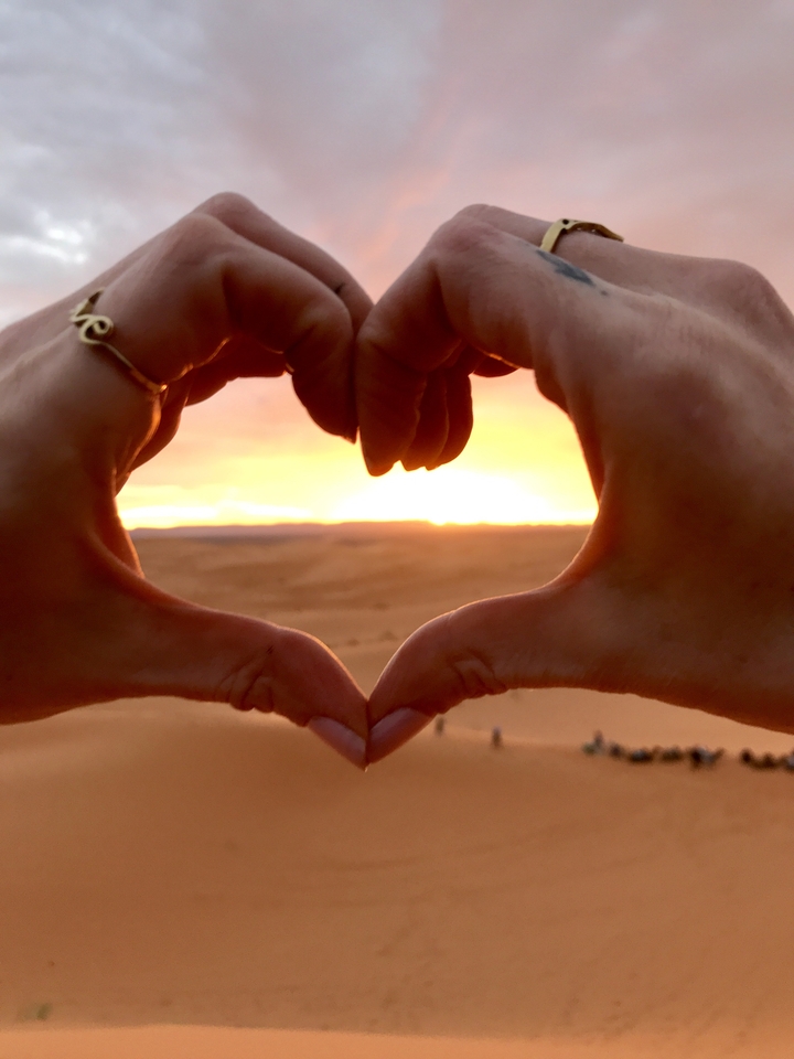 Hands forming a heart shape with a sunset in the background.