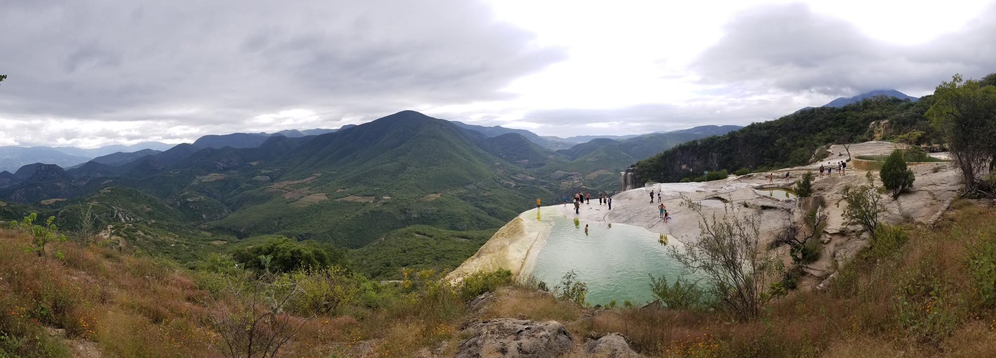 Vue panoramique sur la montagne avec un bassin naturel en roche et des personnes à proximité.