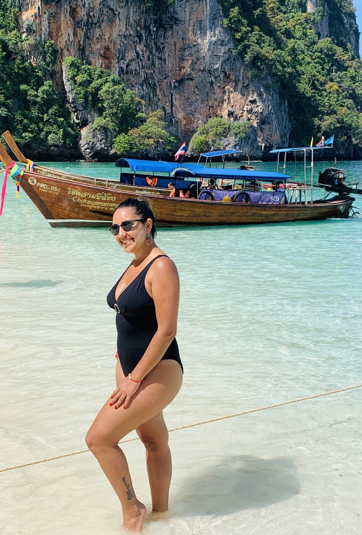 Woman standing in shallow water with a traditional boat in the background.