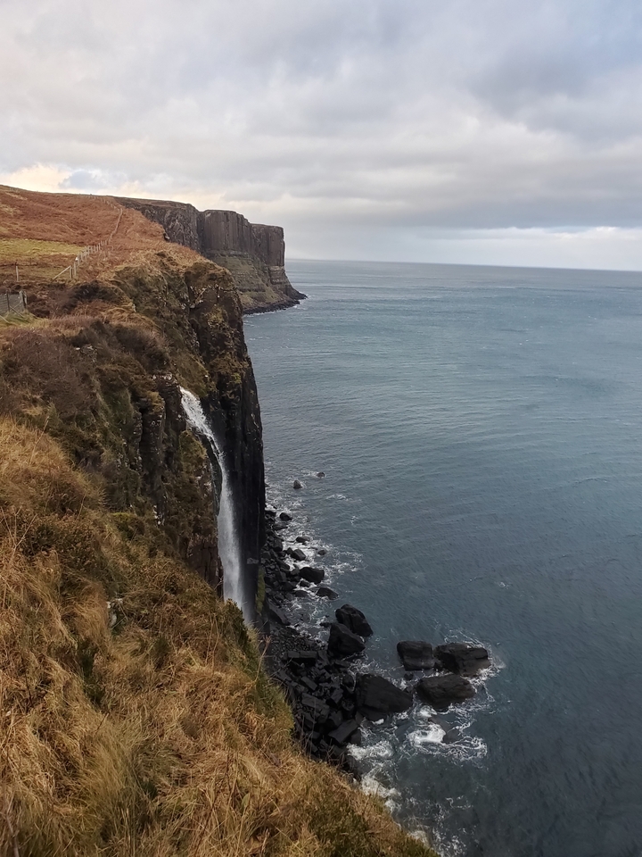 A waterfall cascading down a rugged coastline into the sea.