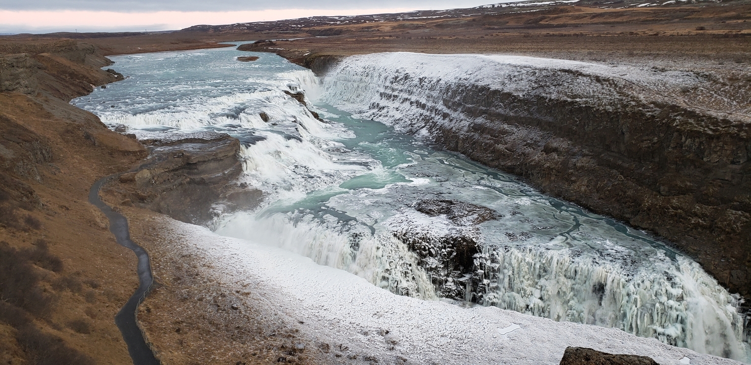 Wide view of a waterfall surrounded by snow-covered cliffs.