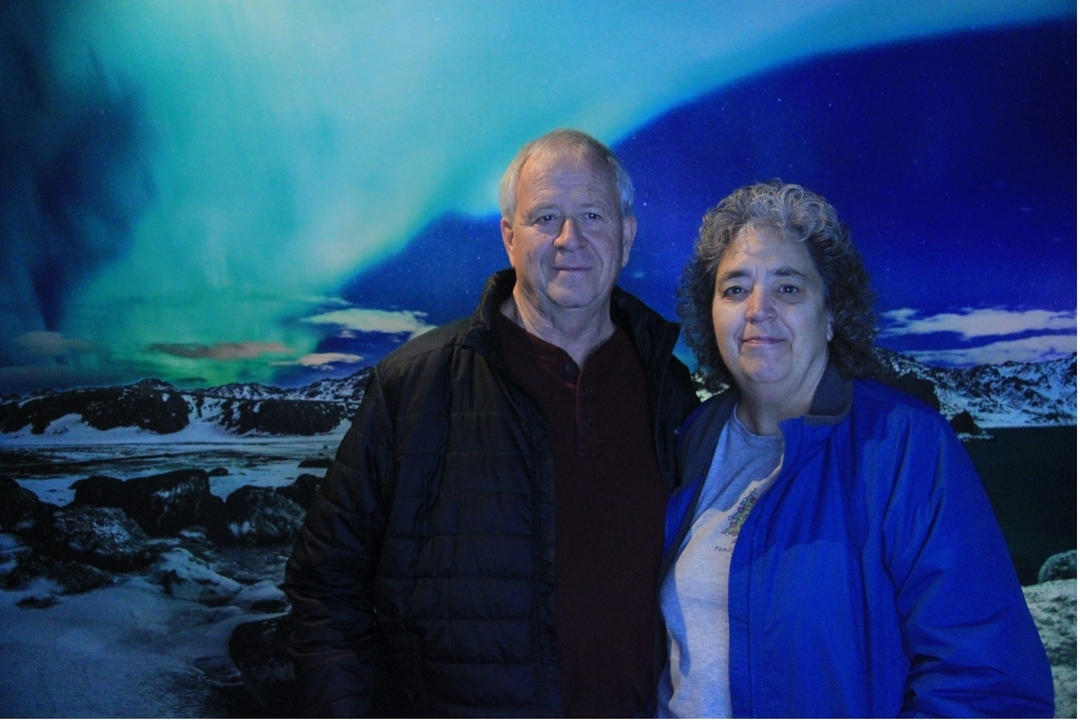 Two people posing with the Northern Lights in the background.