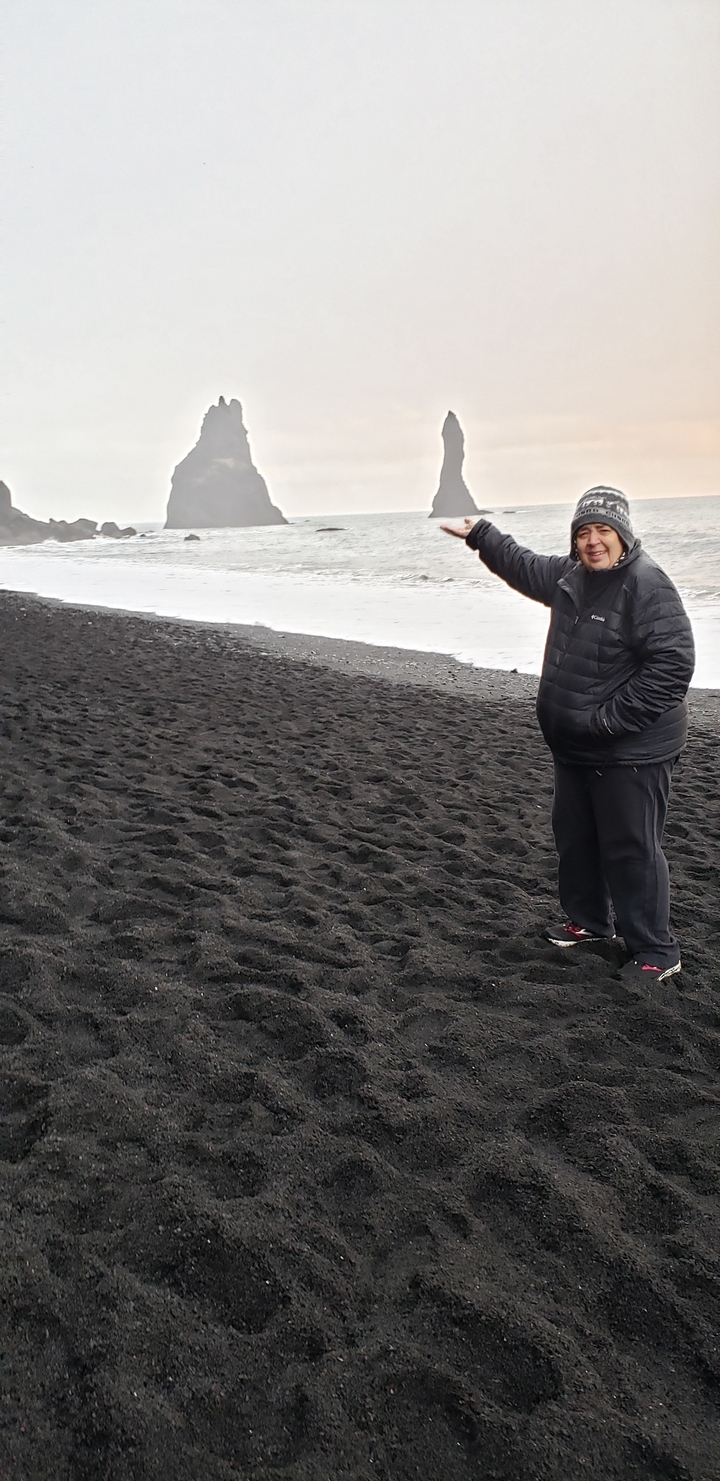 Person standing on a black sand beach.