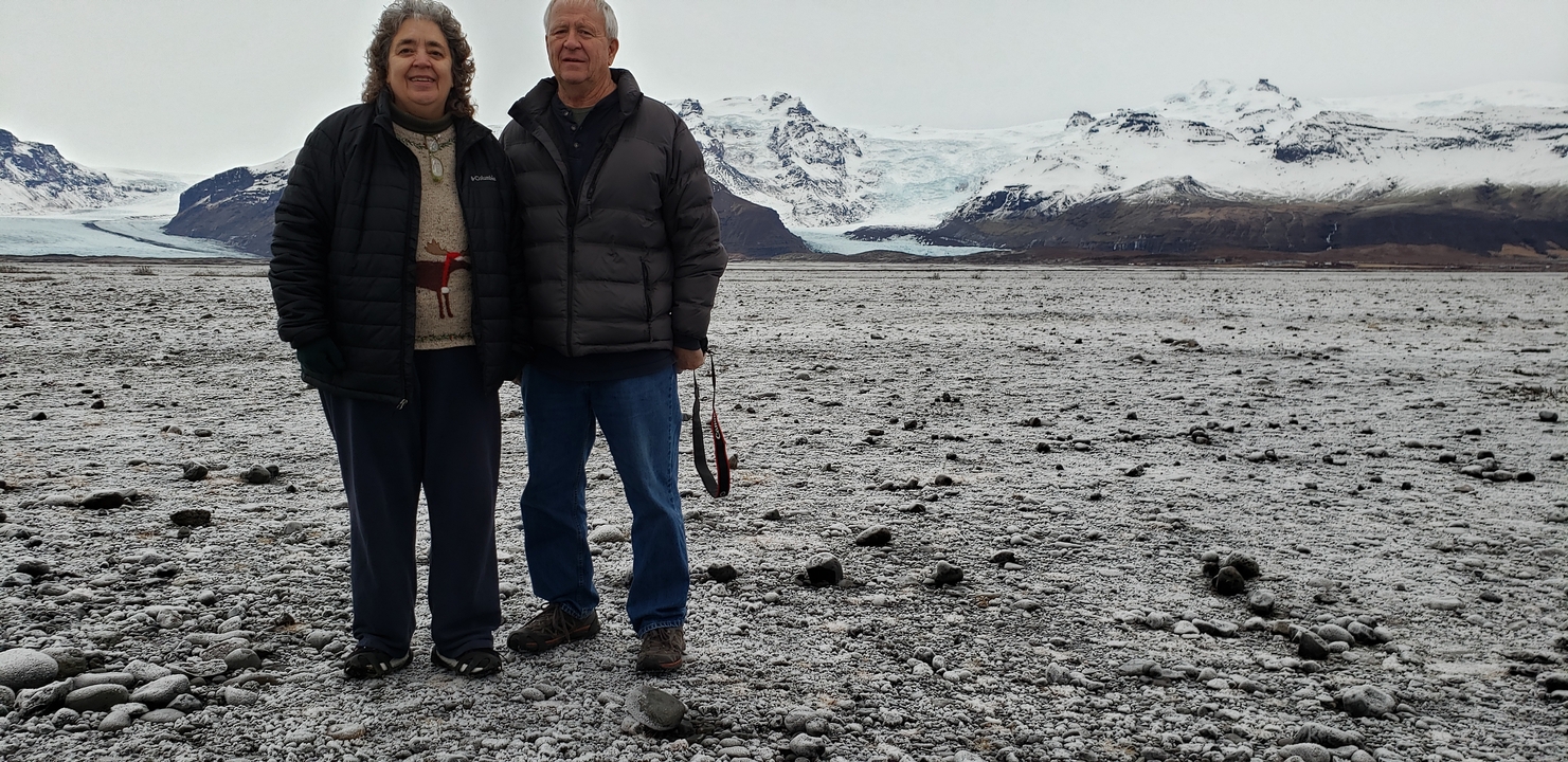 Couple standing on icy terrain with glacial mountains behind.