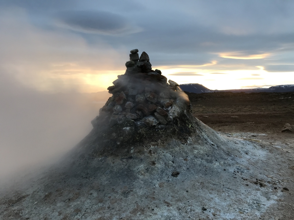 A geothermal hot spring with steam rising, captured at sunset.