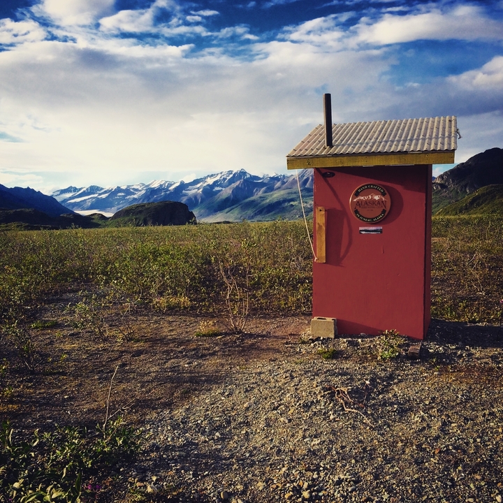 A small wooden building in a field with mountains in the background.