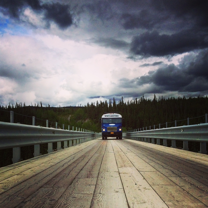 A blue bus on a wooden bridge surrounded by dense forest.