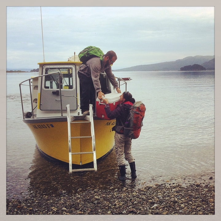 Two people transferring gear from a small yellow boat.