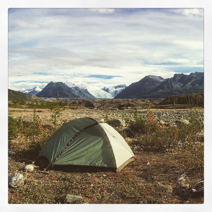 A tent set up in a rocky landscape with a glacier in the distance.