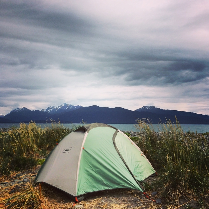 A tent set up by a lake with mountains in the background.