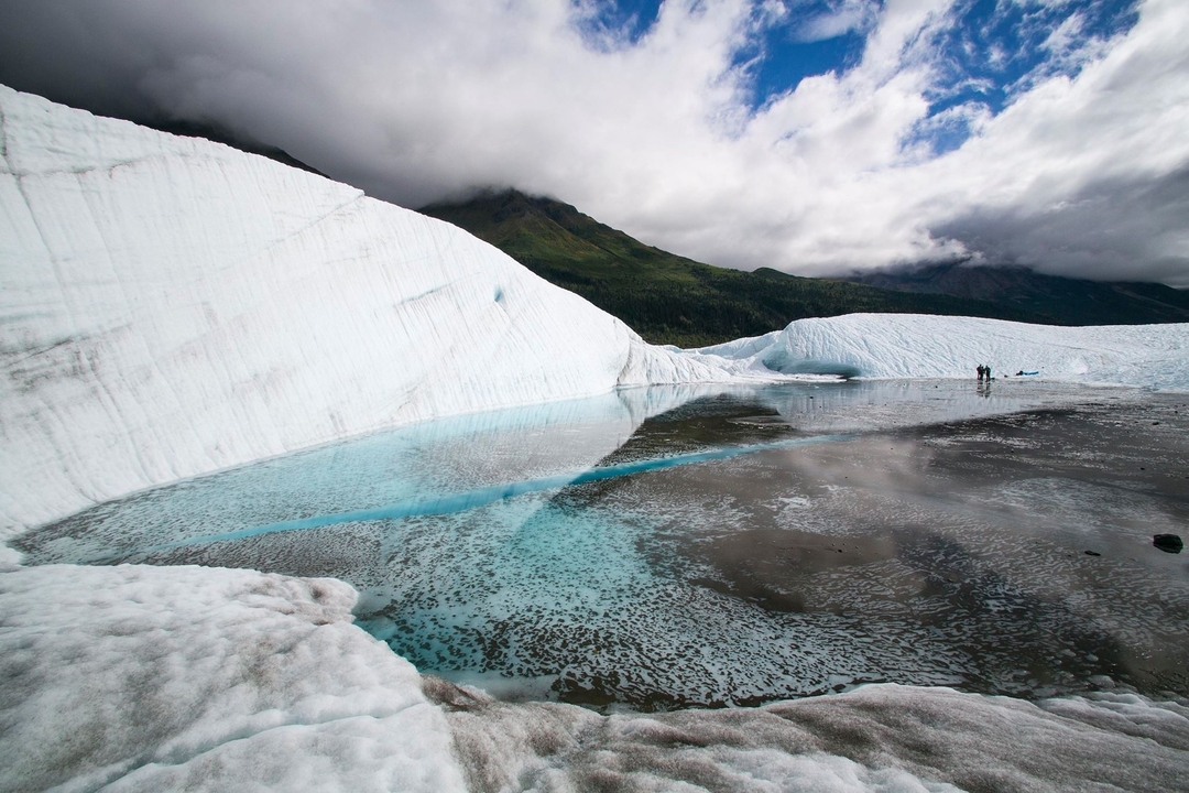 Glacial ice formation with clear blue ice pool and snowy peaks.