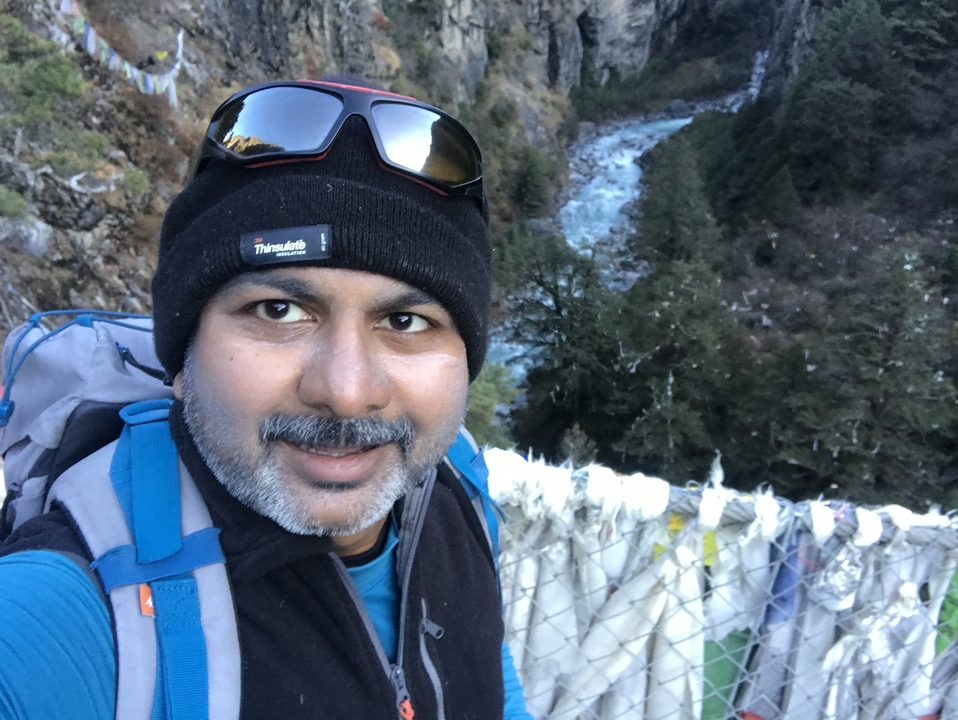 Personne prenant un selfie sur un pont avec une rivière et des arbres en contrebas.