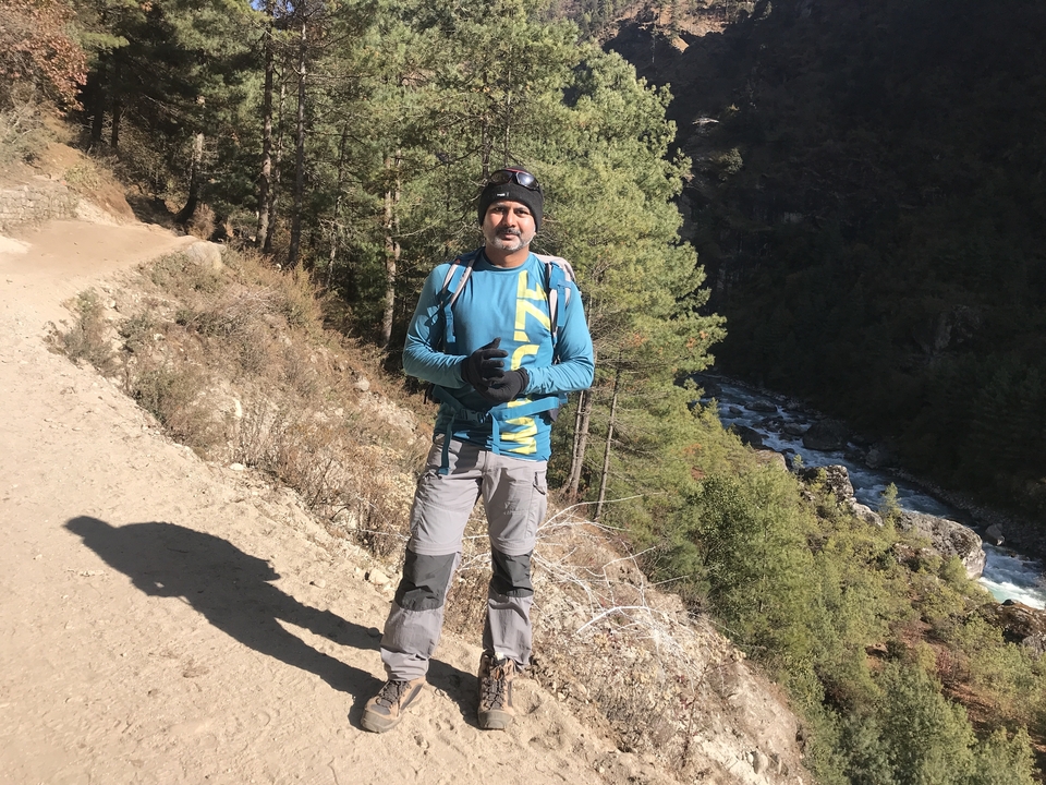 Homme debout sur un sentier avec une rivière et une forêt en arrière-plan.
