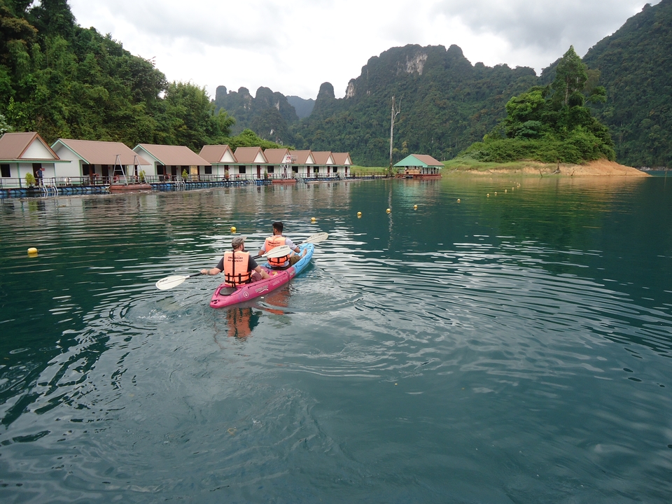 Two people kayaking on a lake with floating bungalows.