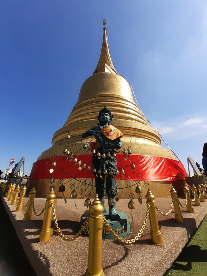 Golden statue with decorative bells and a large golden stupa in the background.