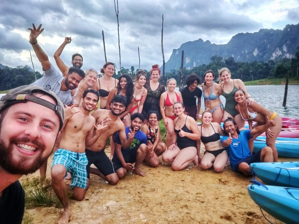 Group photo by a lake with mountains in the background.