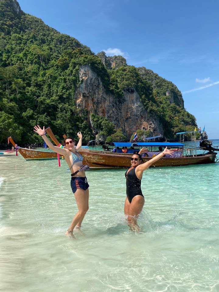 Two women posing in water with a traditional boat in the background in Thailand.