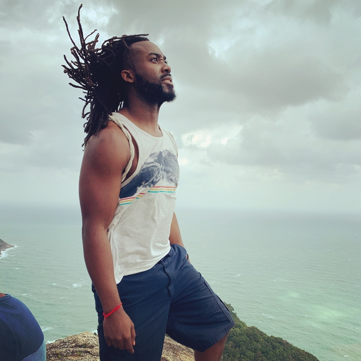 Person standing on a cliff overlooking the ocean on a cloudy day.
