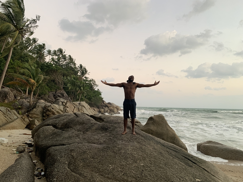 Man standing on rocks by the ocean with open arms.