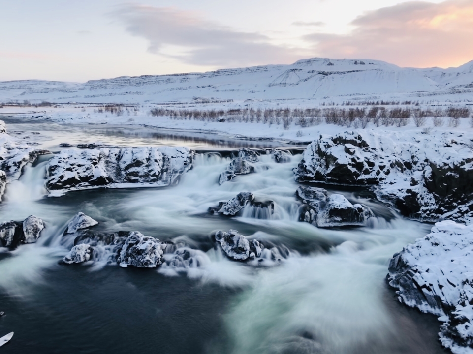 Snowy waterfall surrounded by rocky terrain.