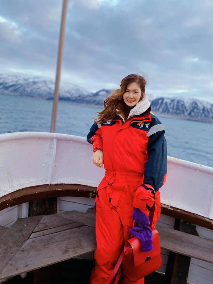 Person in a red winter suit standing on a boat with icy mountains in the background.