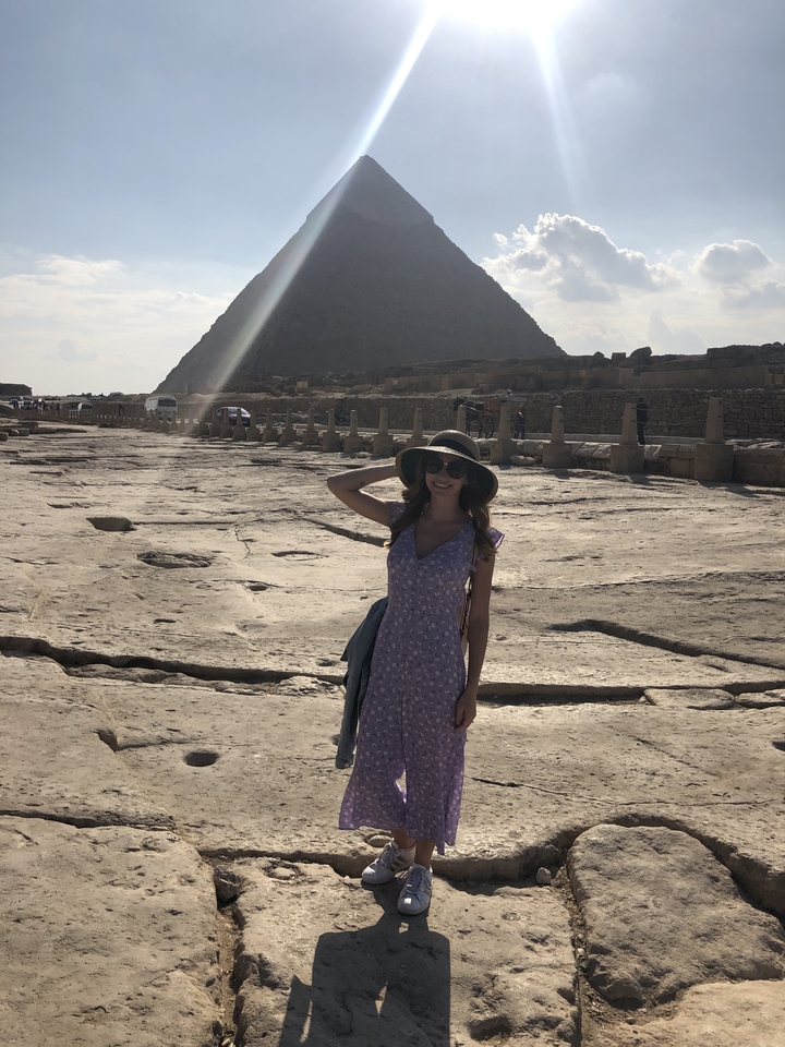 Woman posing with her hand raised in front of an ancient pyramid.