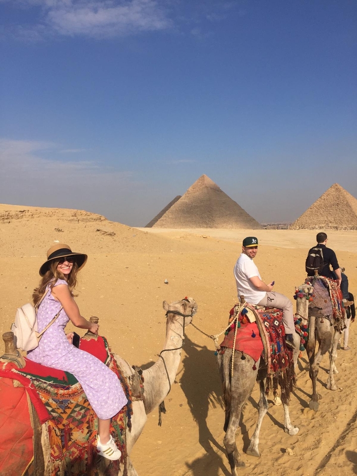 People riding camels with pyramids in the background.