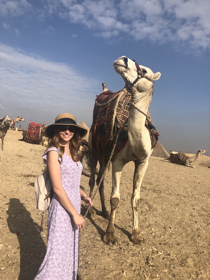 Woman posing with a camel and pyramids in the background.
