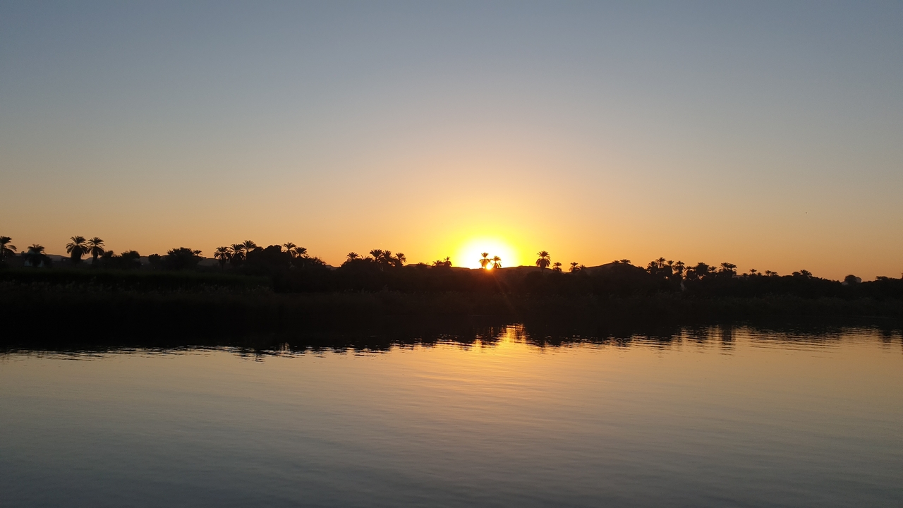 Sunset over a river with silhouetted trees.