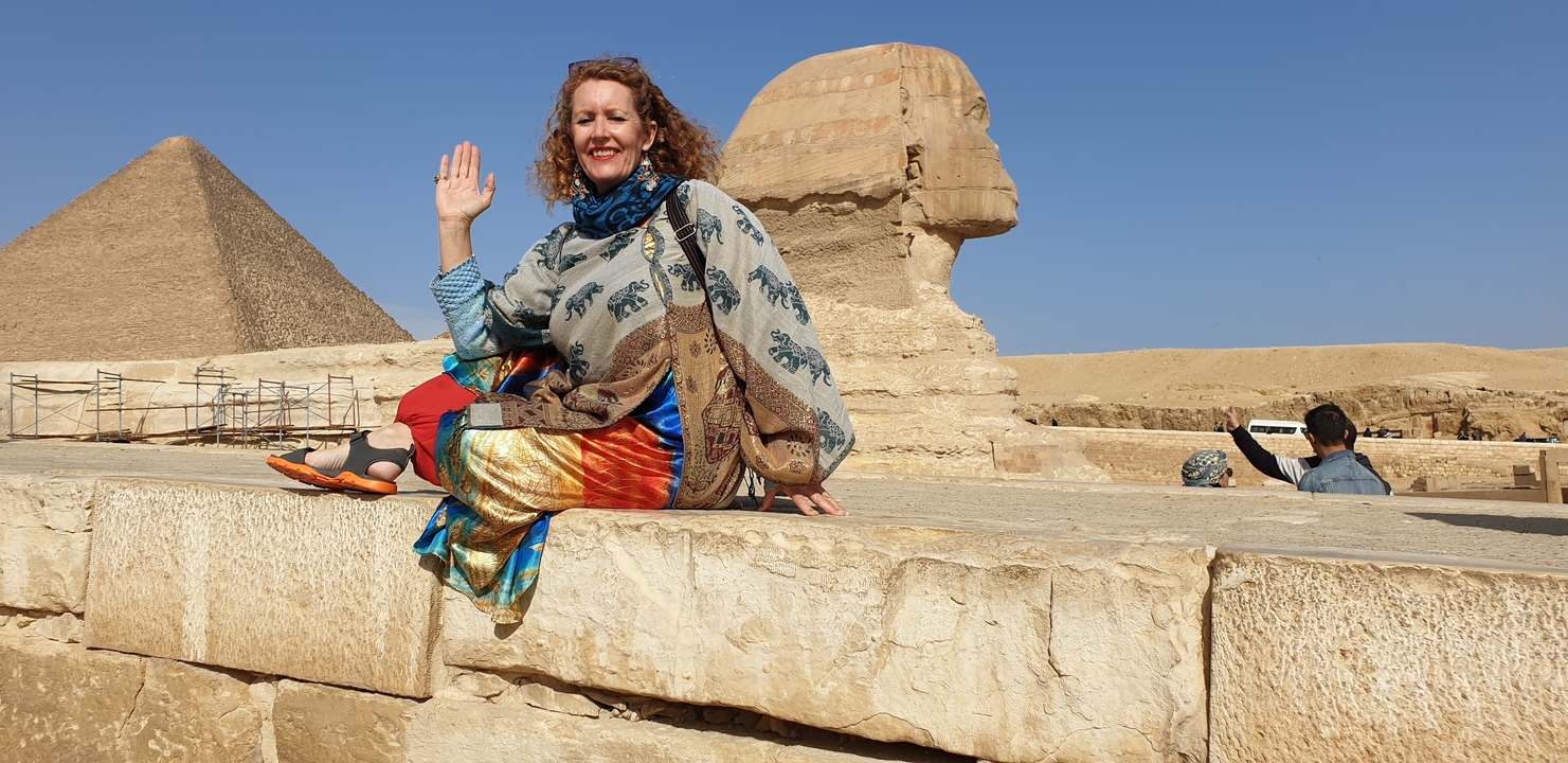 Woman sitting near the Sphinx and pyramids posing.