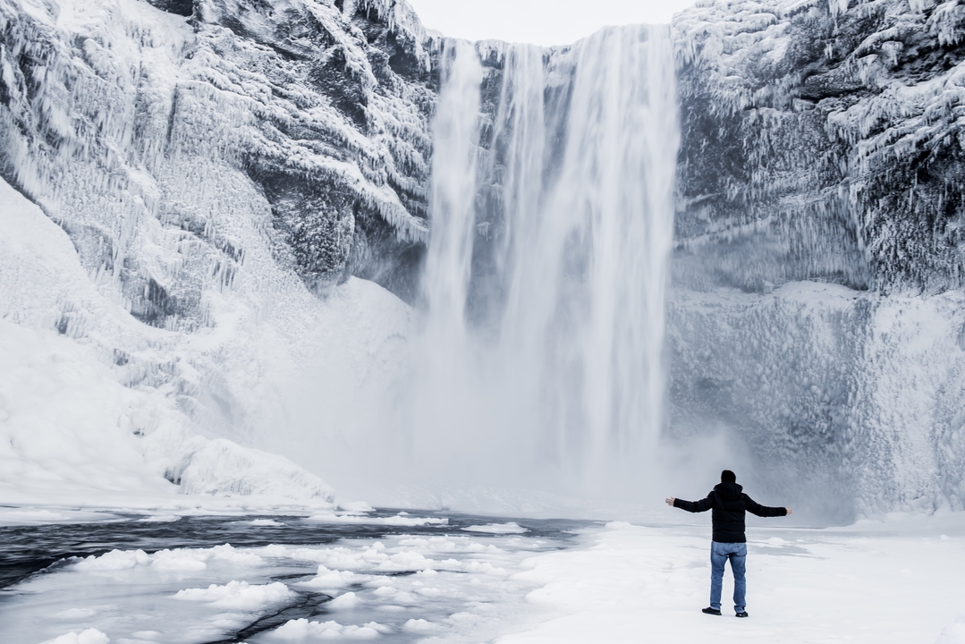 Person standing in front of a large snowy waterfall.