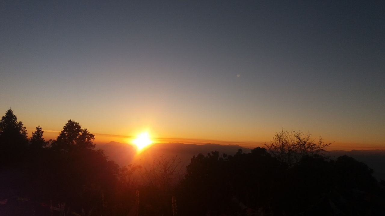Lever de soleil sur les montagnes avec des arbres au premier plan.