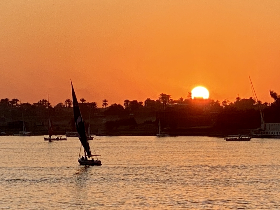Voiliers sur une rivière avec un coucher de soleil en arrière-plan.