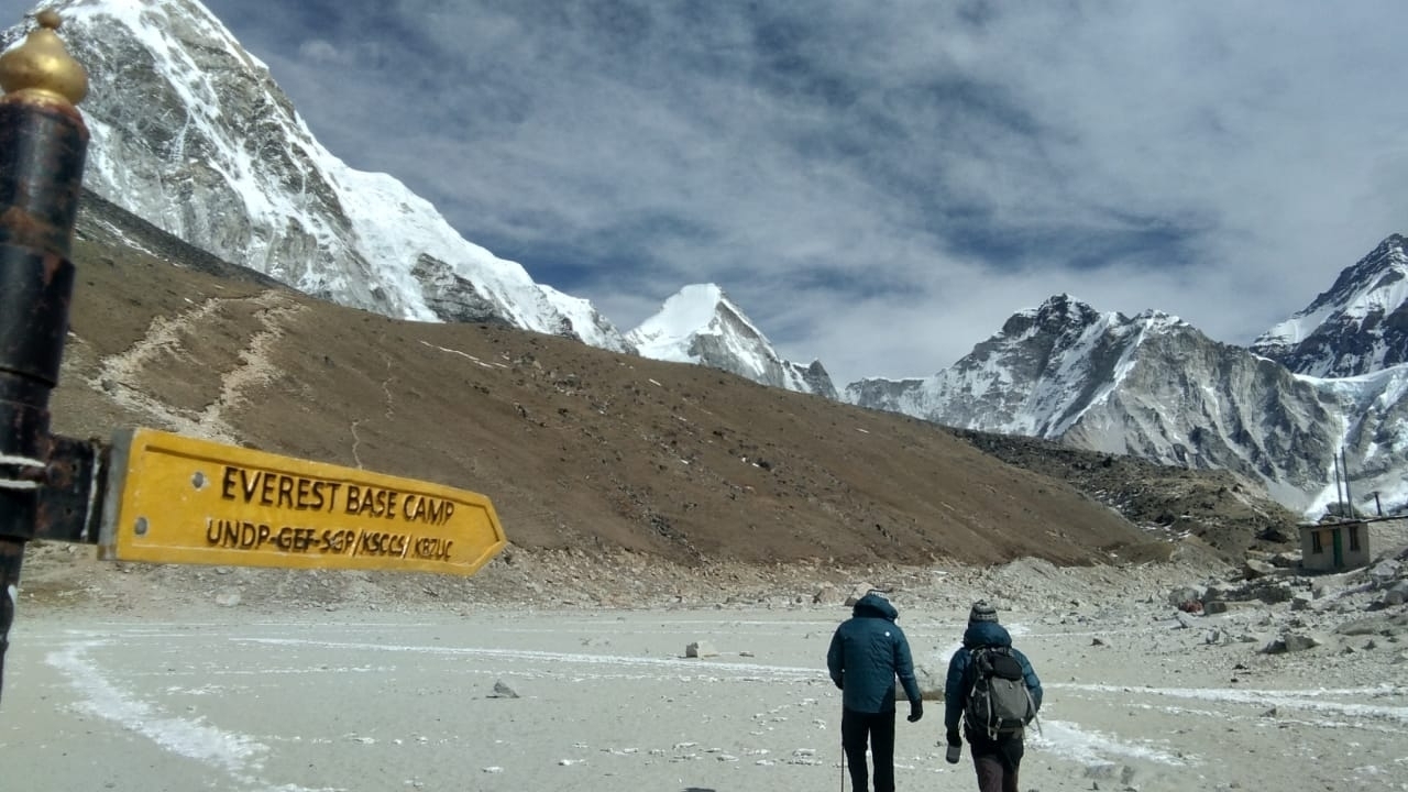 Hikers walking towards Everest Base Camp sign on a rocky path.
