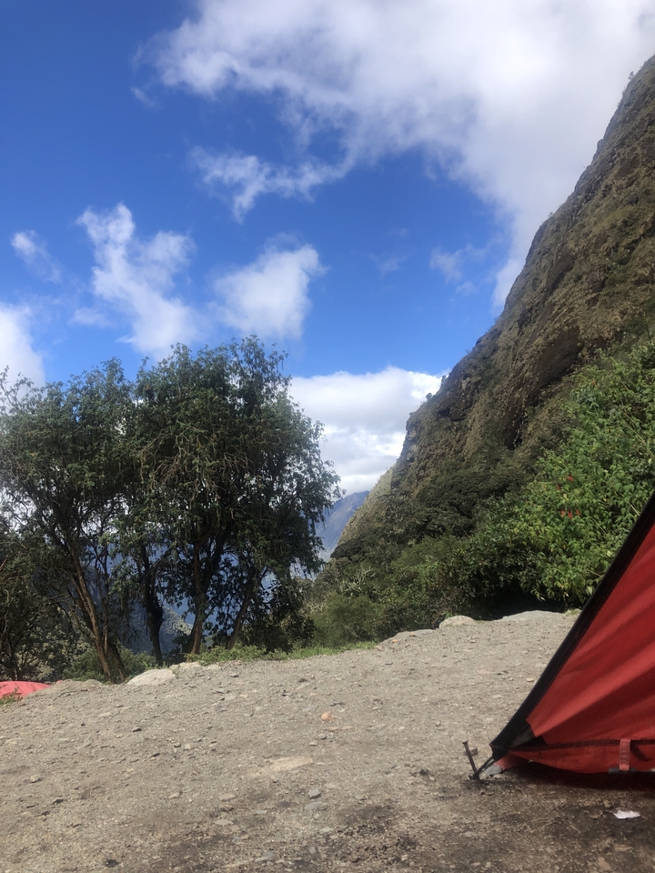 Flanc de montagne bordé d'arbres sous un ciel partiellement nuageux.