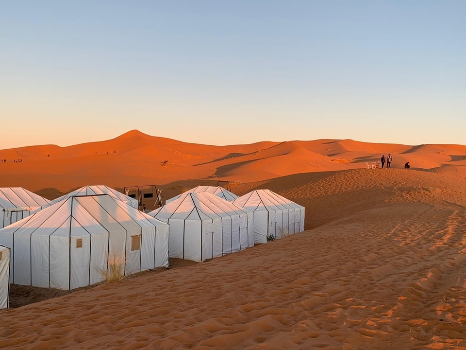 Luxury desert camp with white tents on sand dunes.