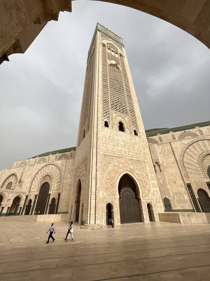 Tall mosque minaret with intricate designs against a cloudy sky.