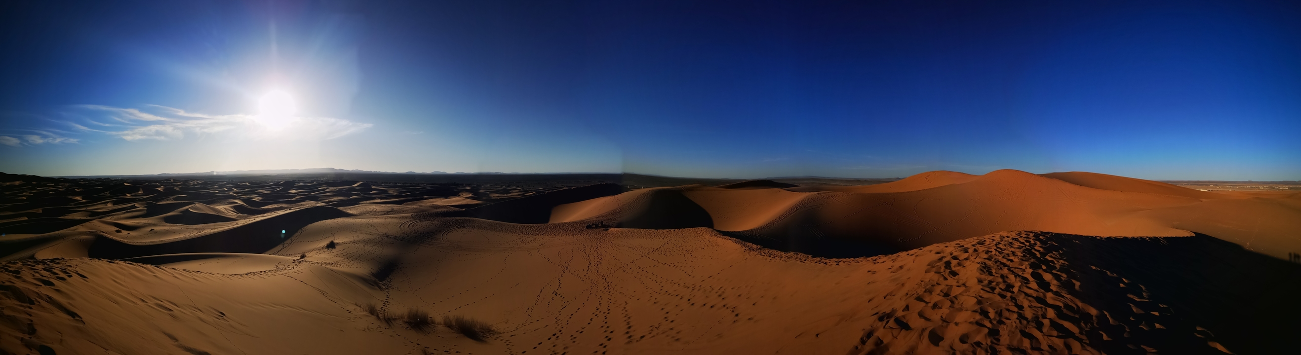 Vast desert landscape with rolling sand dunes under a blue sky.