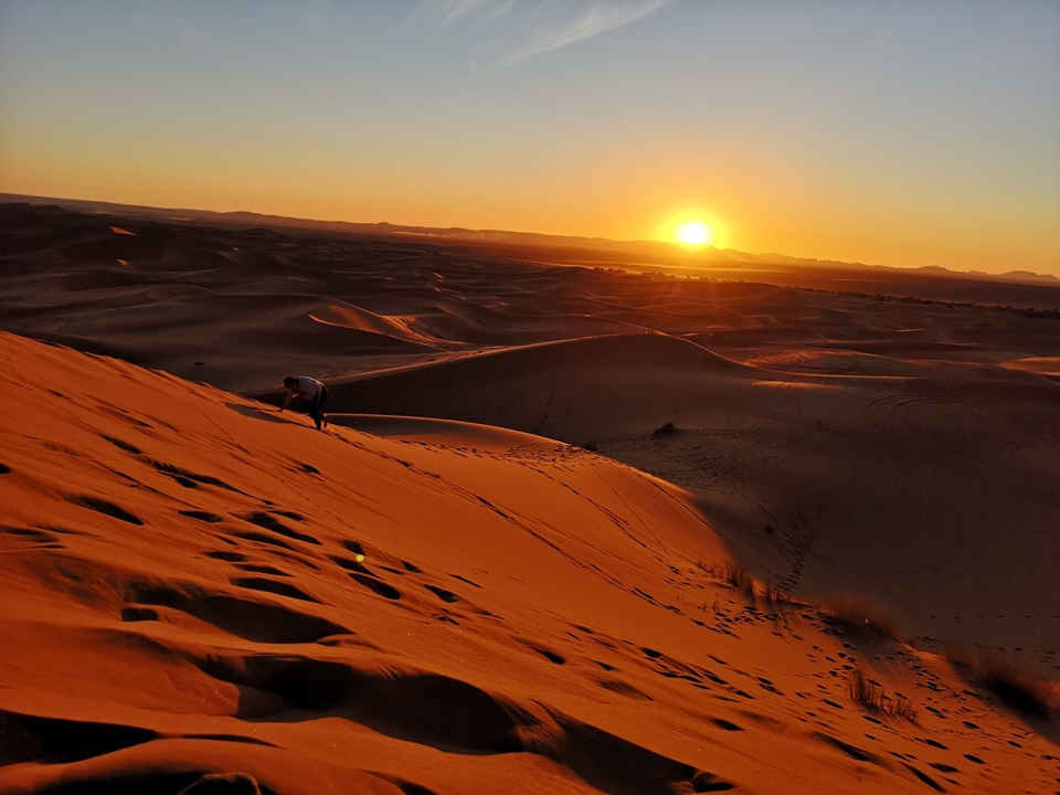 Person climbing a sand dune during sunset.