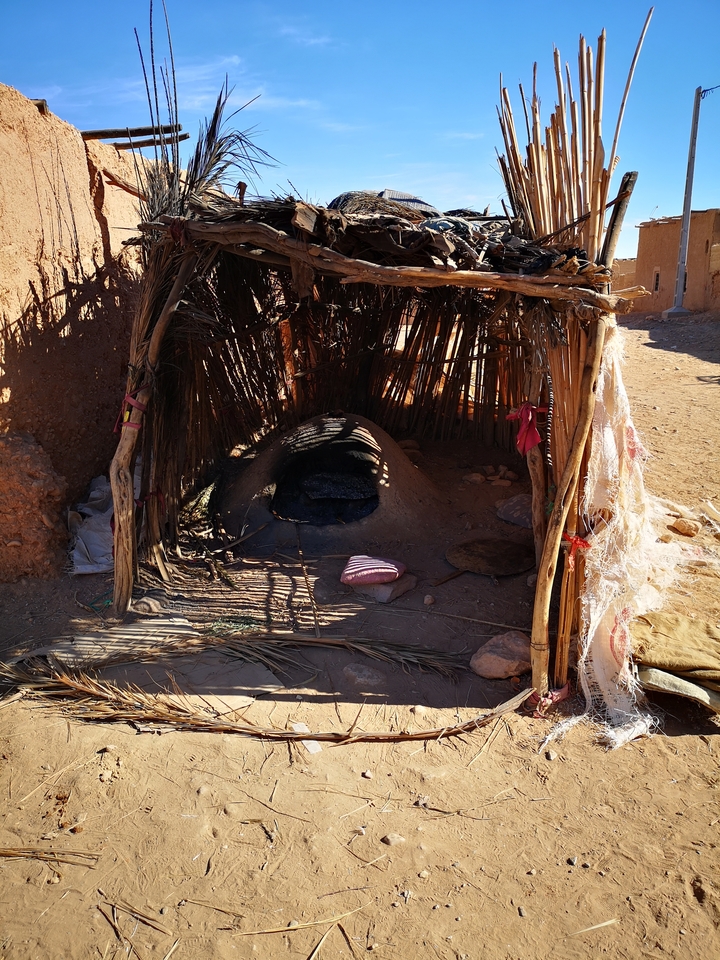 Earth oven sheltered by a rustic structure made of wood and straw.