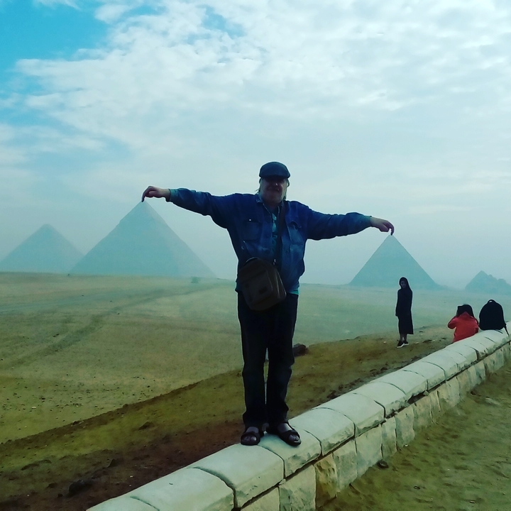 Personne posant les bras étendus devant les pyramides.