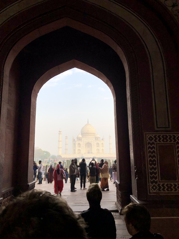 Foules observant le Taj Mahal depuis une entrée voûtée.
