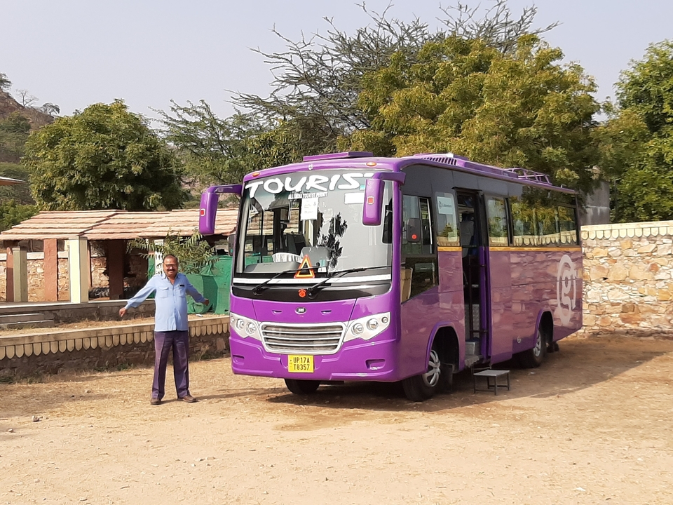 Homme posant avec un bus touristique violet.