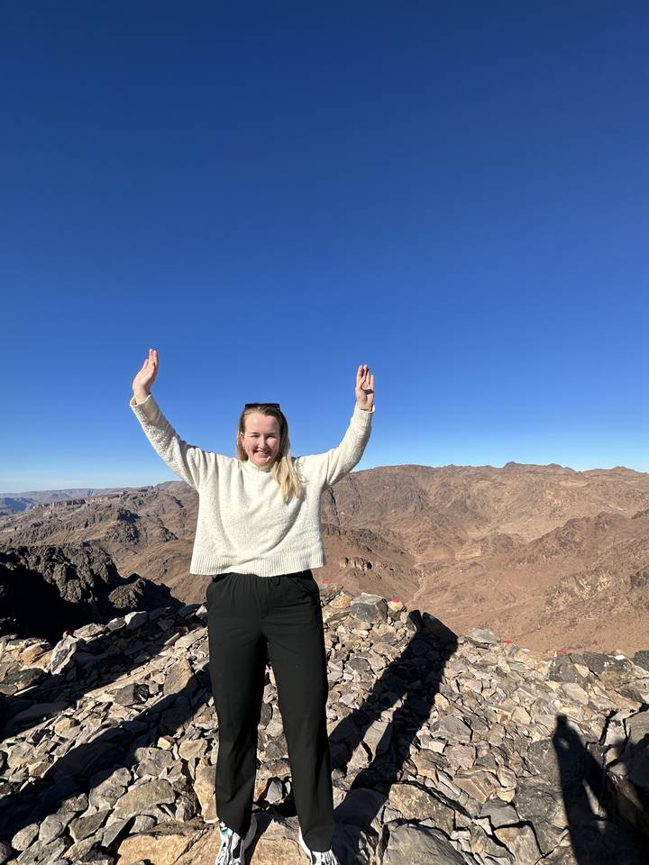 Persoon die op rotsachtig terrein staat met opgeheven armen.