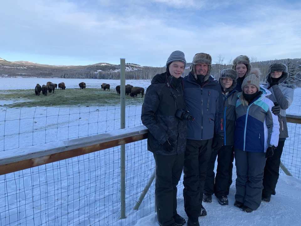 A family group standing by a fence, with bison in the snowy background.